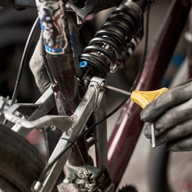 Cropped shot of male mechanic working in bicycle repair shop, repairing mountain bike using special tool, wearing protective gloves