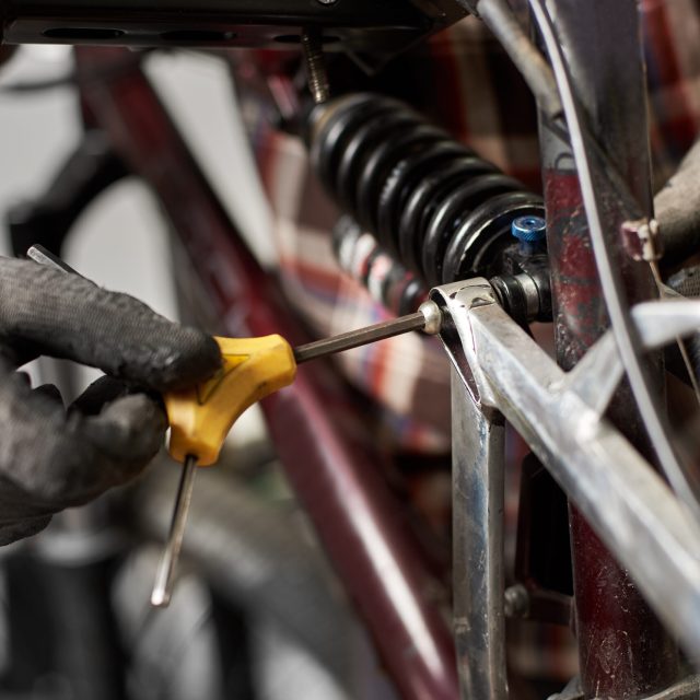Cropped shot of man mechanic working in bicycle repair shop, worker repairing mountain bike using special tool, wearing protective gloves